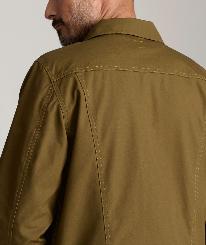 Model is wearing UNTUCKit Rizzo waxed trucker jacket in dark olive. 