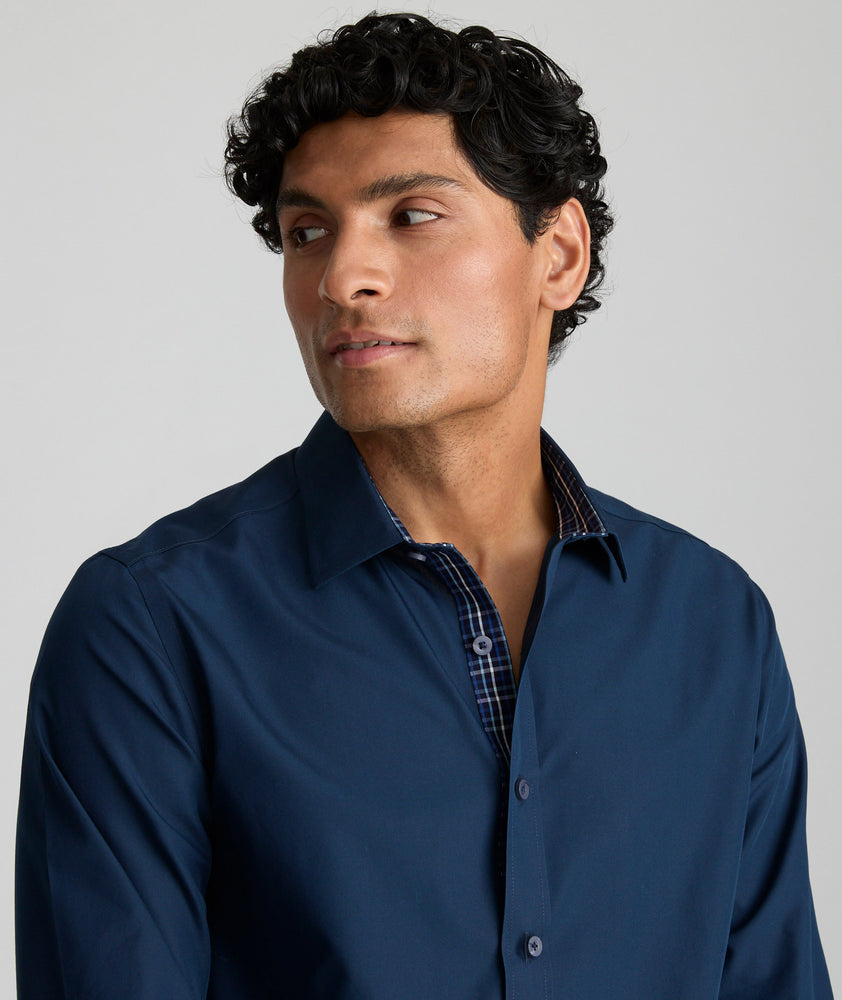 Model is wearing UNTUCKit Roberts wrinkle-free shirt in solid navy with blue check contrast cuff. 